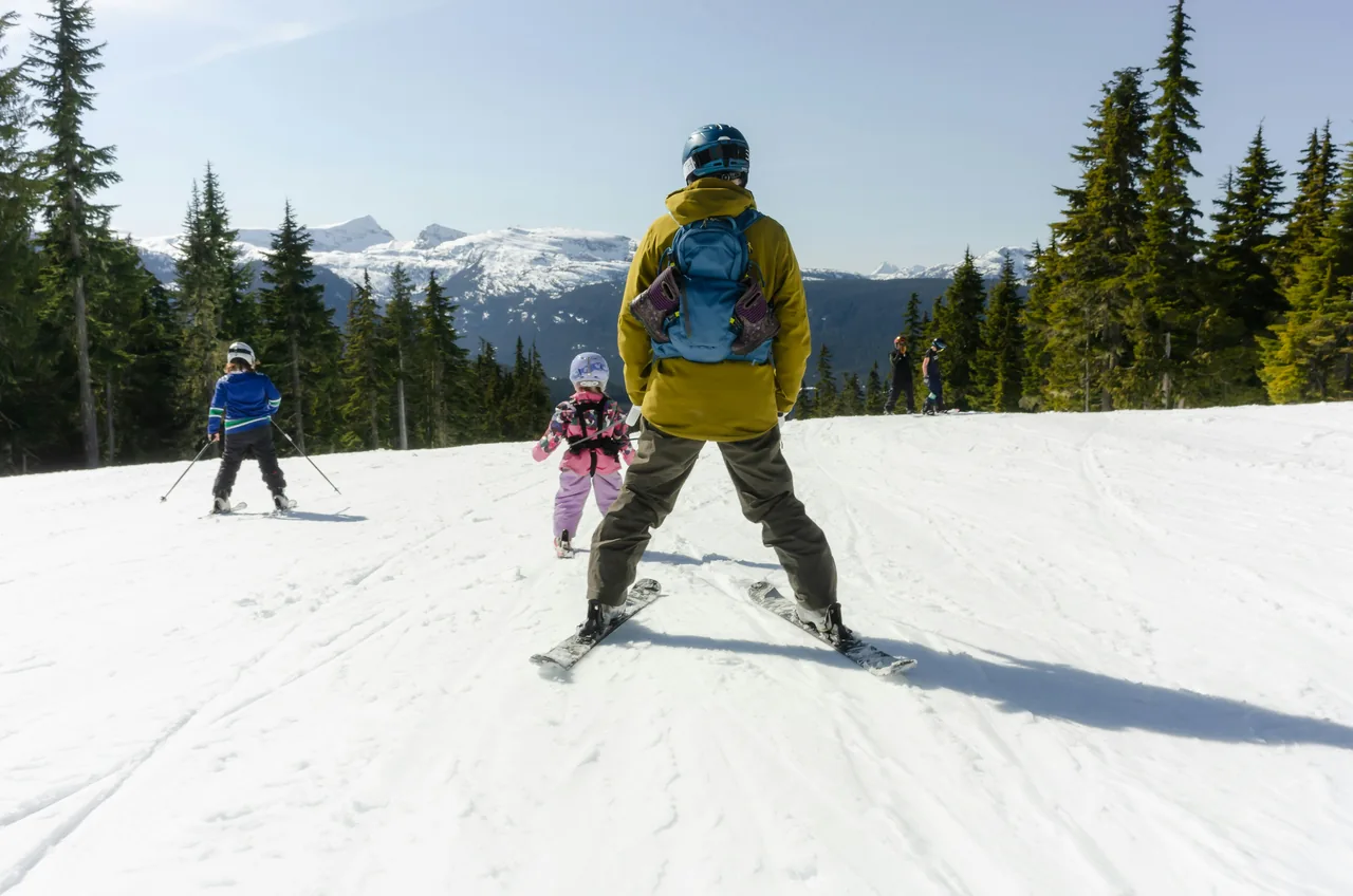 A man and two children skiing on a mountain