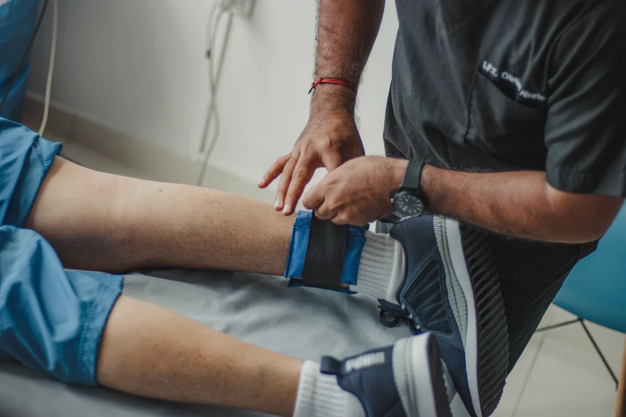 A physiotherapist adjusts a leg strap on a patient in a clinical setting
