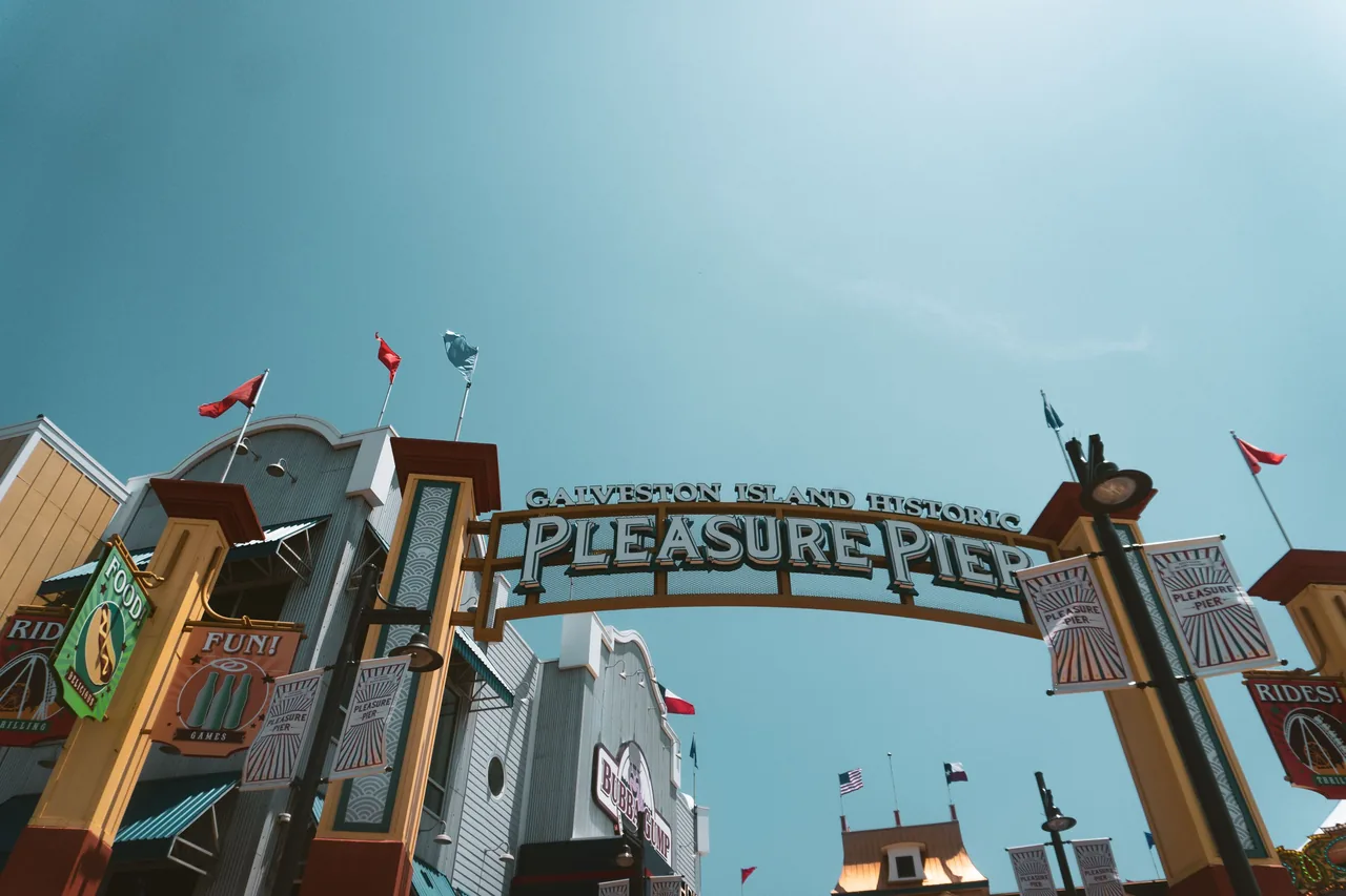View of the iconic Galveston Island Historic Pleasure Pier entrance under a bright blue sky