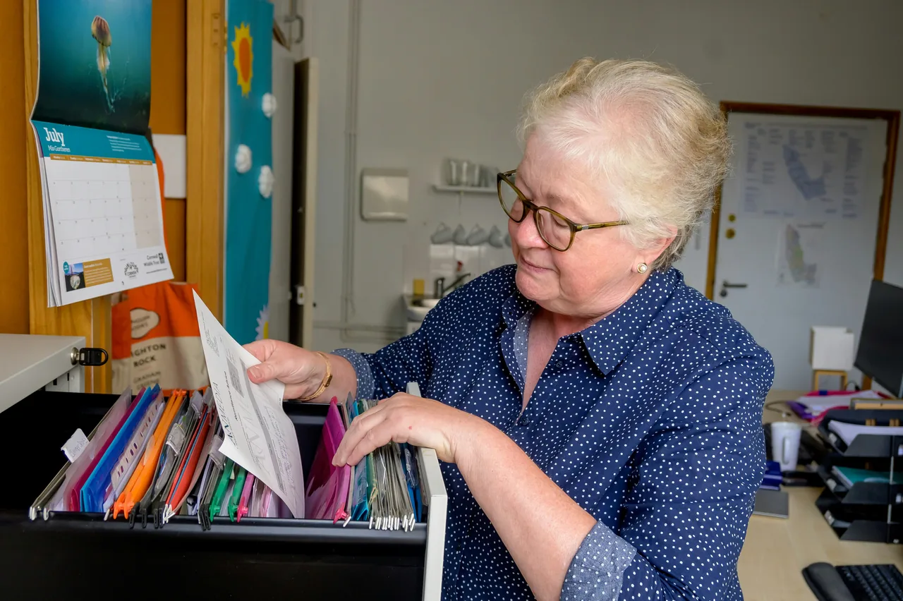 An older woman working, pulling out some files from a drawer